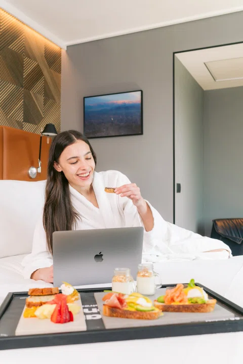 Mujer trabajando con notebook junto a desayuno en cama.