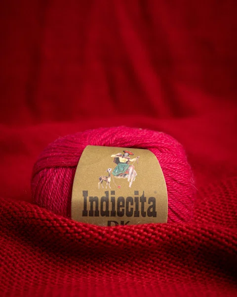Ovillo fucsia con etiqueta sobre tela roja.