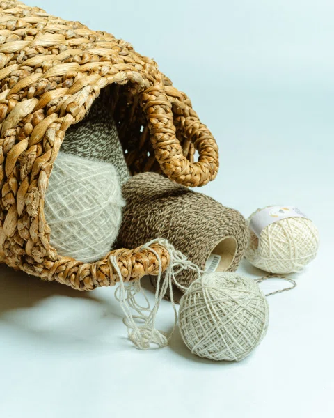 Ovillos de lana junto a tejido artesanal beige.