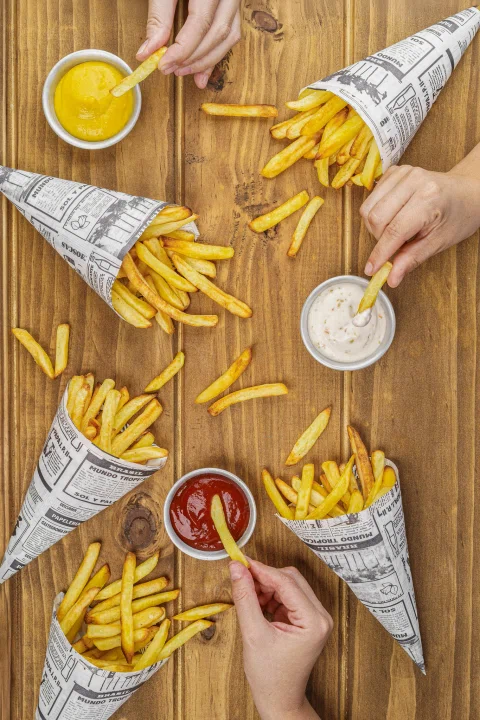 Papas fritas servidas en conos de papel con varias salsas.