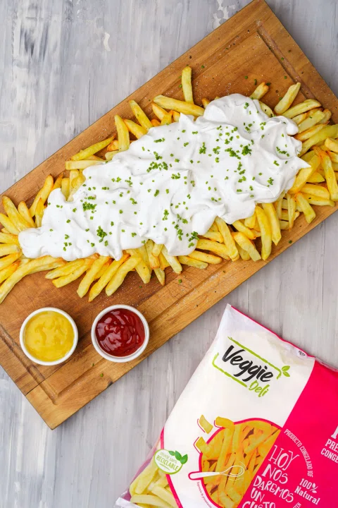 Papas con salsa blanca sobre tabla y envase Veggie Deli.