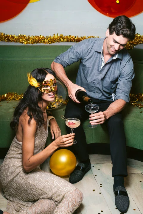 Pareja celebrando con botella y globos.