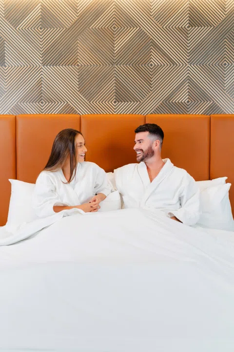 Pareja conversando sobre cama de hotel.