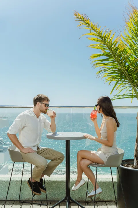 Pareja conversando en terraza frente al mar.