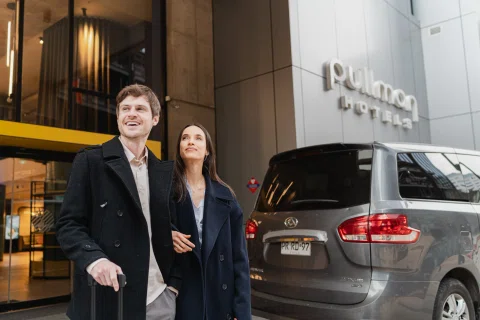 Pareja llegando al hotel junto a vehículo.