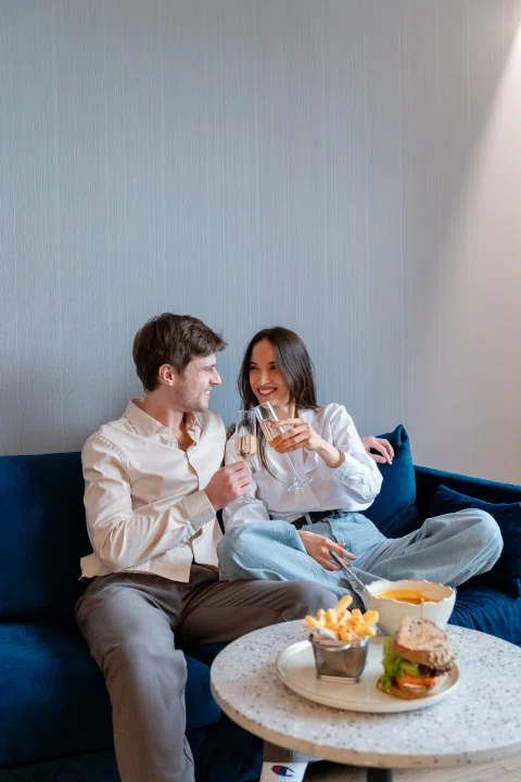 Pareja sentada en sofá compartiendo aperitivo.