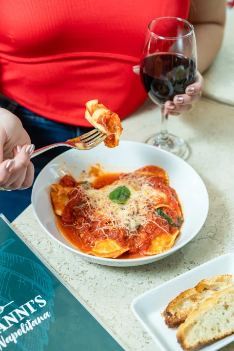 Persona comiendo pasta con salsa roja y copa de vino.