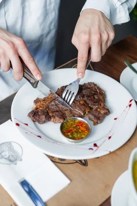 Persona cortando carne servida con acompañamientos.