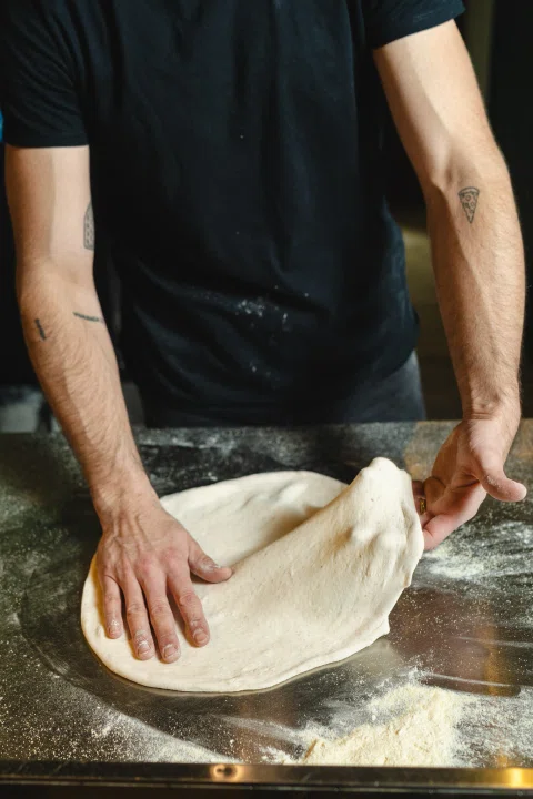 Persona estirando masa de pizza sobre mesón.