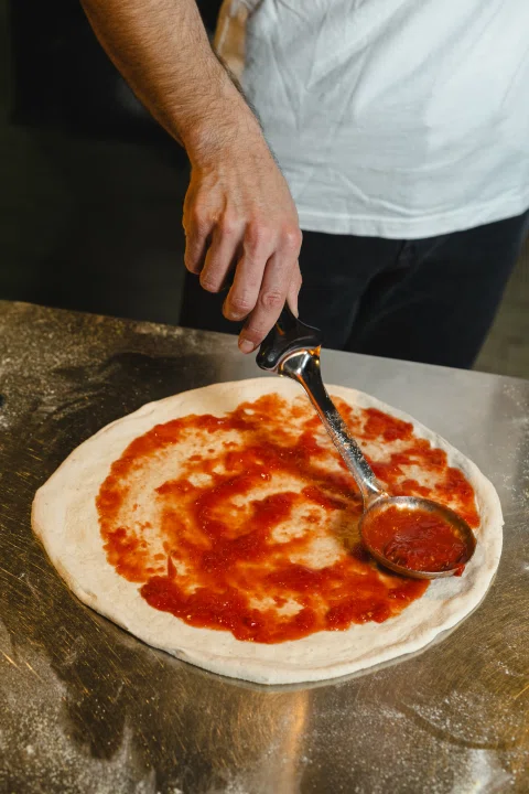 Persona extendiendo salsa de tomate sobre masa.