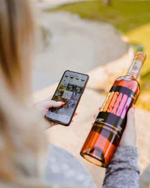 Persona fotografiando botella de vino rosado con teléfono.