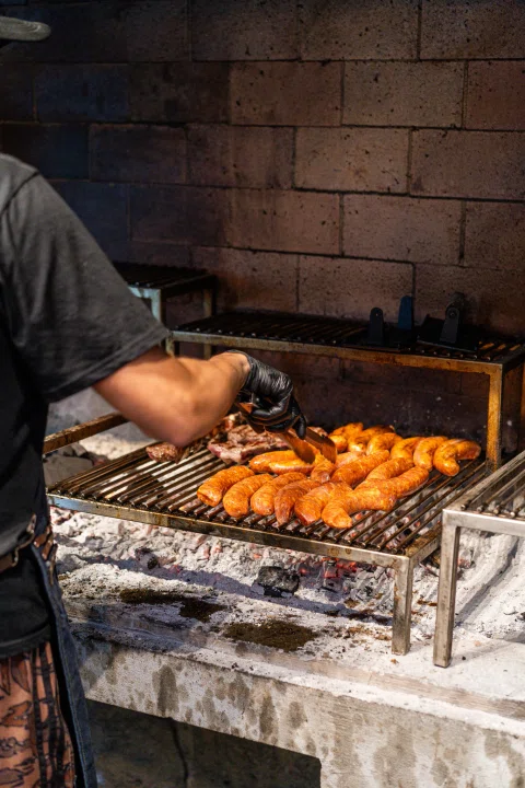 Persona manipulando carnes en la parrilla.