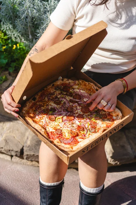 Persona mostrando pizza dentro de caja abierta al exterior.