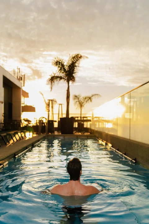 Persona nadando en piscina exterior al atardecer.