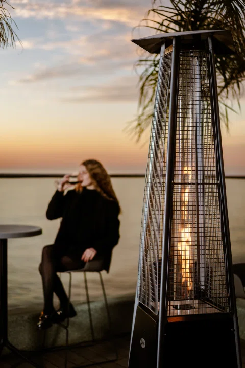 Persona sentada junto a calefactor en terraza al atardecer.