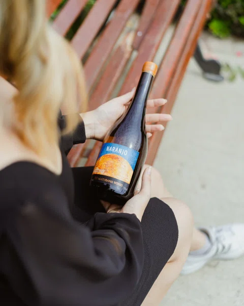 Persona sentada sosteniendo botella de vino con etiqueta azul.