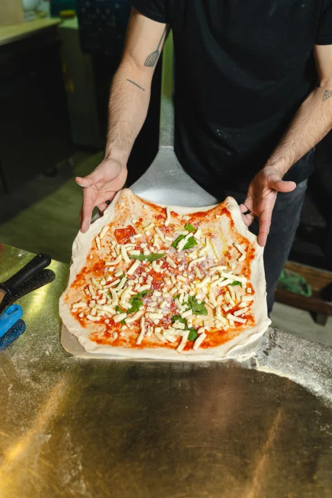 Persona sosteniendo pizza con ingredientes frescos.