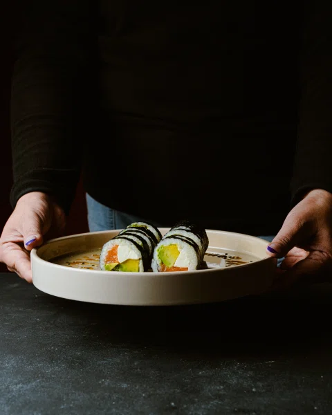 Persona sosteniendo plato con rolls de sushi.