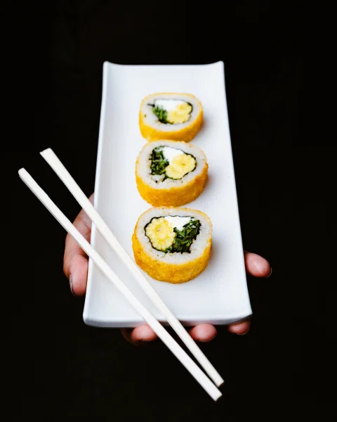 Persona sosteniendo plato con tres piezas de sushi.