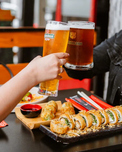 Personas brindando con cervezas sobre mesa de sushi.