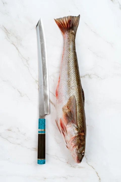 Pescado abierto junto a cuchillo sobre fondo blanco.
