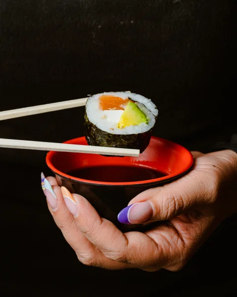 Pieza de sushi con salmón sostenida sobre recipiente de salsa.