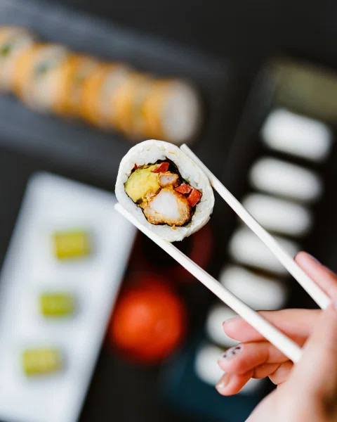 Pieza de sushi sostenida con palillos en primer plano.