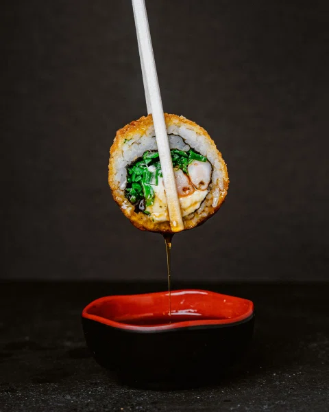 Pieza de sushi suspendida sobre salsa con palillos.