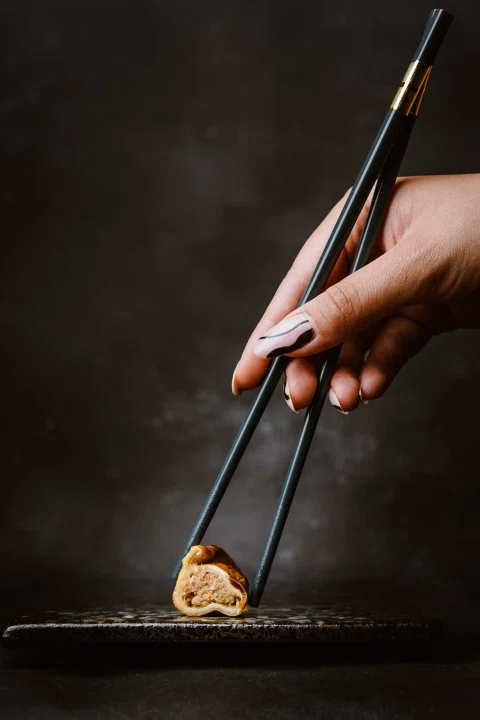 Pinzas sostienen un bocado gastronómico sobre fondo oscuro.