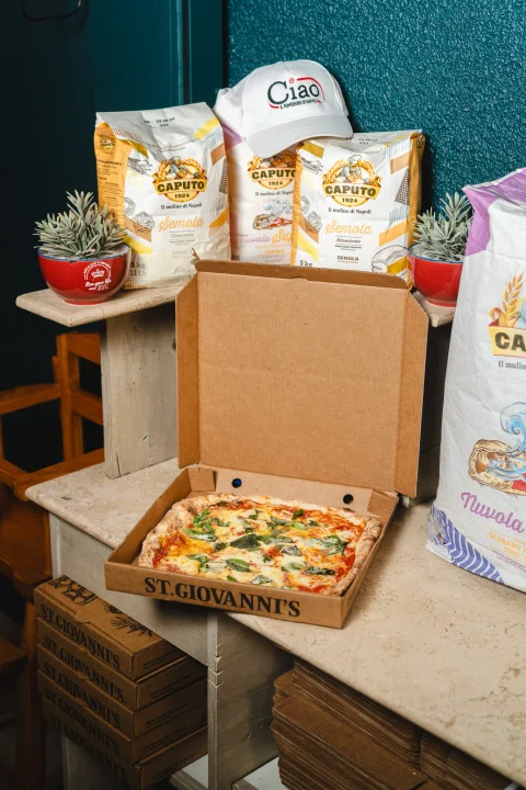 Pizza en caja abierta junto a sacos de harina.