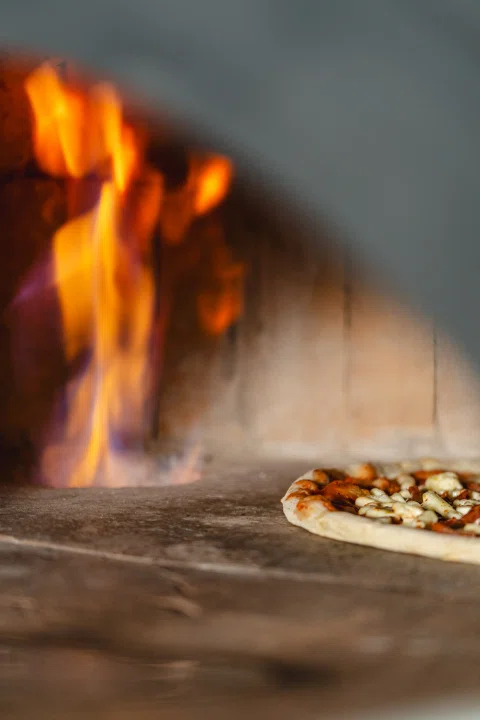 Pizza cocinándose junto a fuego del horno.