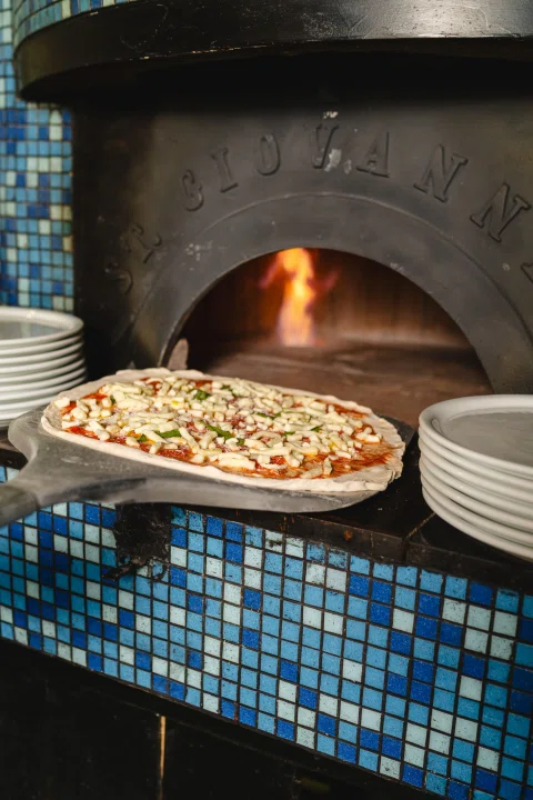 Pizza dentro de horno de piedra encendido.