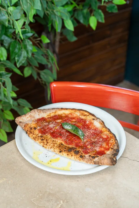 Pizza individual servida sobre plato con hojas verdes.