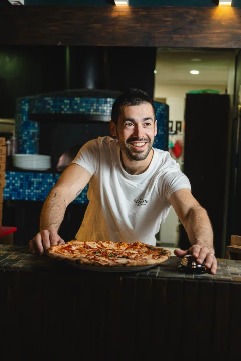 Pizzero sonriendo mientras sostiene pizza.