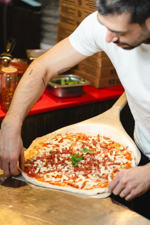 Pizzero sosteniendo pizza preparada frente al mesón.
