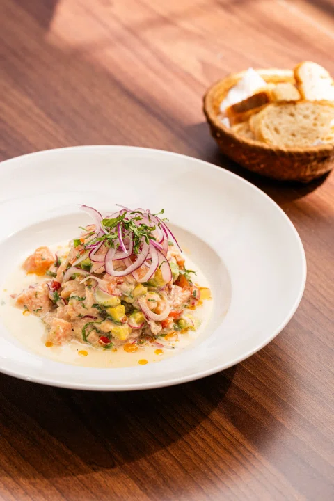 Plato de ceviche con cebolla morada y pan.