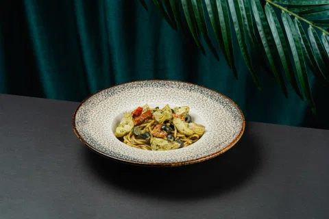 Plato de pasta o risotto con vegetales frente a cortina verde.