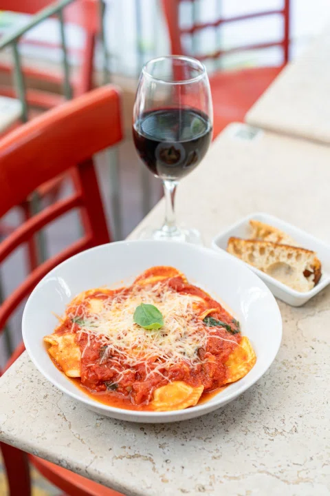 Plato de pasta con salsa roja acompañado de vino.