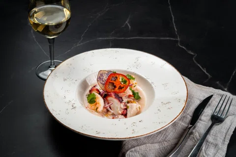 Plato de pescado crudo con vegetales y vino blanco.