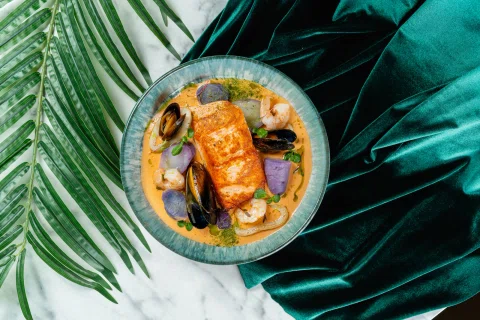 Plato de salmón con vegetales sobre hojas verdes.