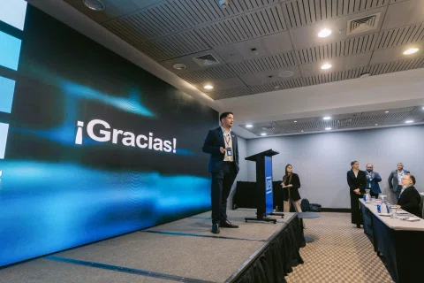 Ponente cierra una presentación frente a una pantalla con mensaje de agradecimiento.
