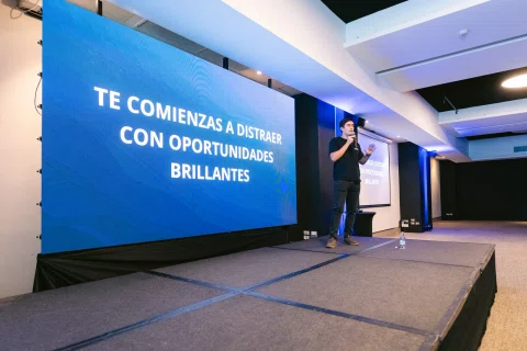 Ponente habla desde el escenario frente a un mensaje proyectado.