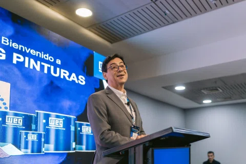 Ponente habla en escenario frente a una pantalla azul.