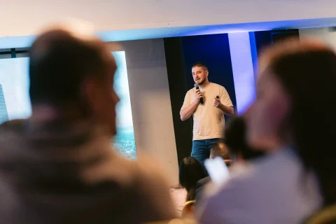 Ponente habla con micrófono visto entre las cabezas del público.