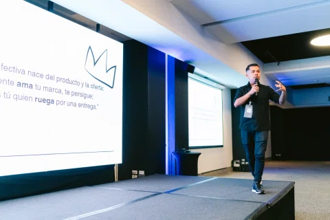 Ponente presenta en escenario frente a una pantalla de proyección.