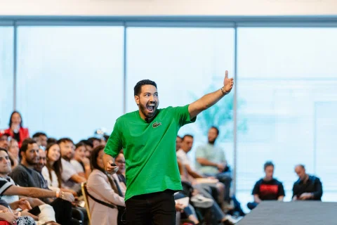 Ponente con camiseta verde habla con micrófono frente al público.