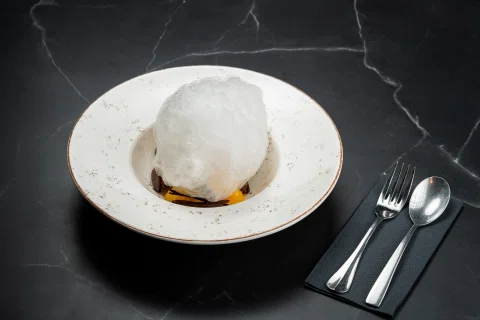 Postre blanco cubierto en plato sobre mesa negra.