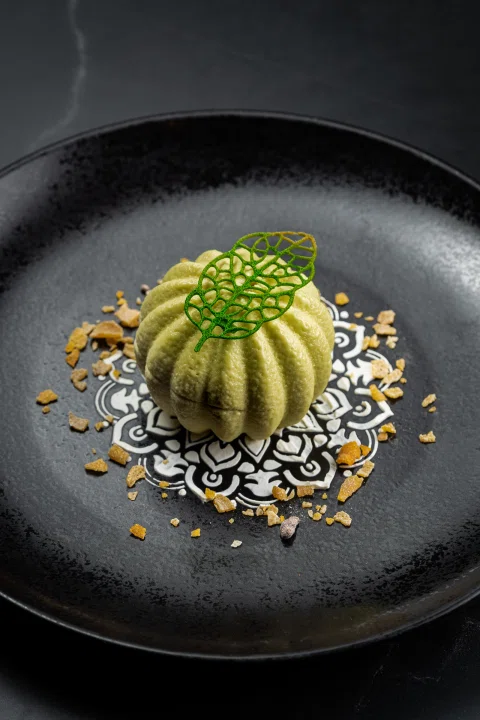 Postre verde en plato negro con decoración.