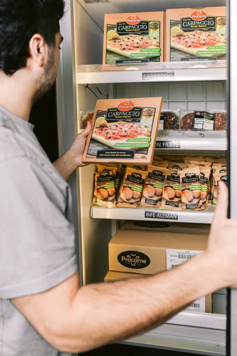 Persona organiza productos congelados en un exhibidor refrigerado.