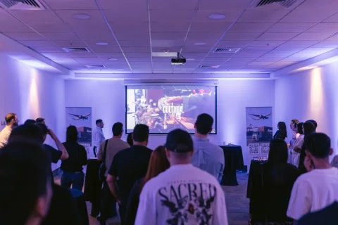 Asistentes observan una actividad en un espacio iluminado en tonos violetas.